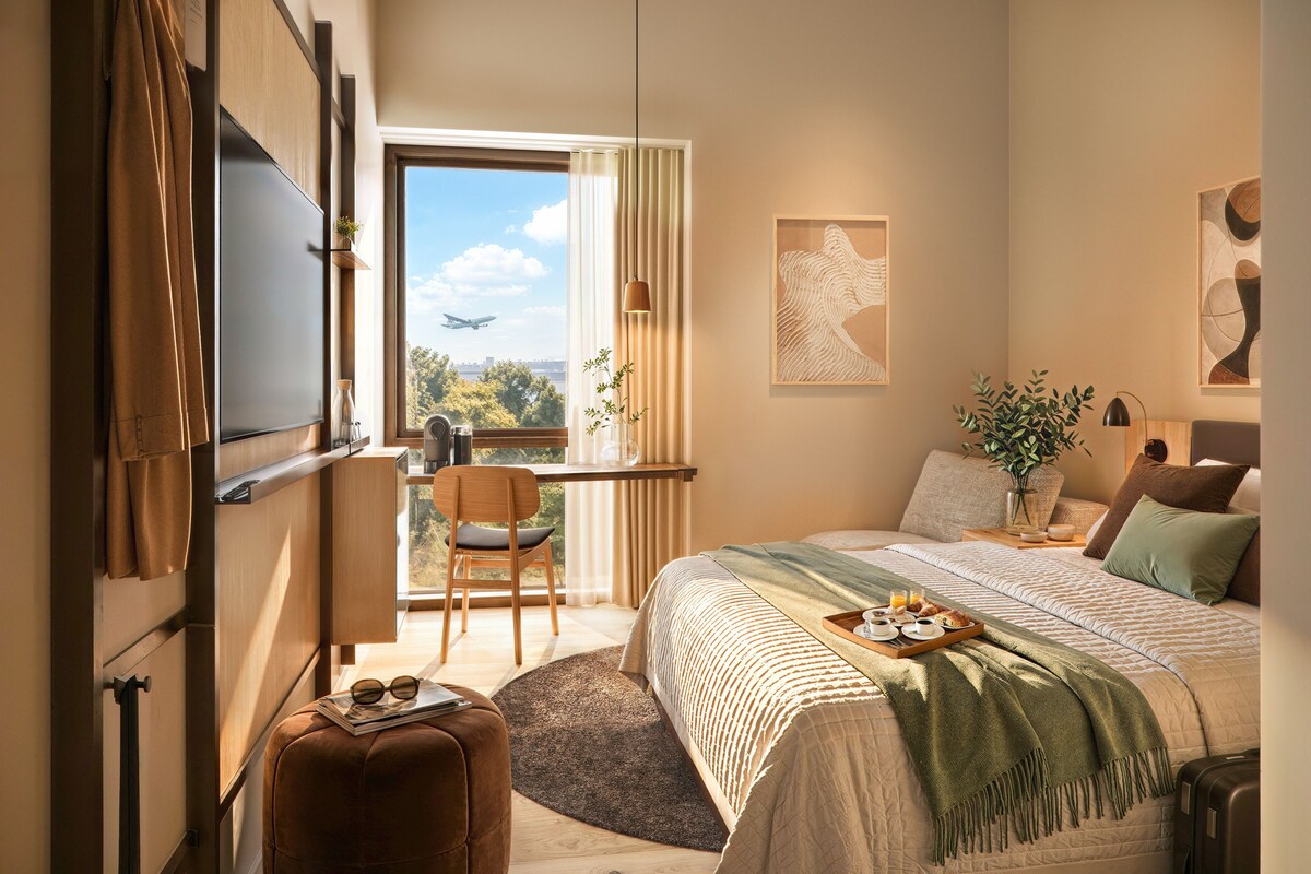 A modern bedroom with a large bed, a desk, and a window with a view of the city.