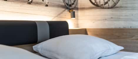 Una cama con almohadillas blancas y un cabecero negro, suelo de madera e imagen de un carruaje antiguo y un caballo en la pared.