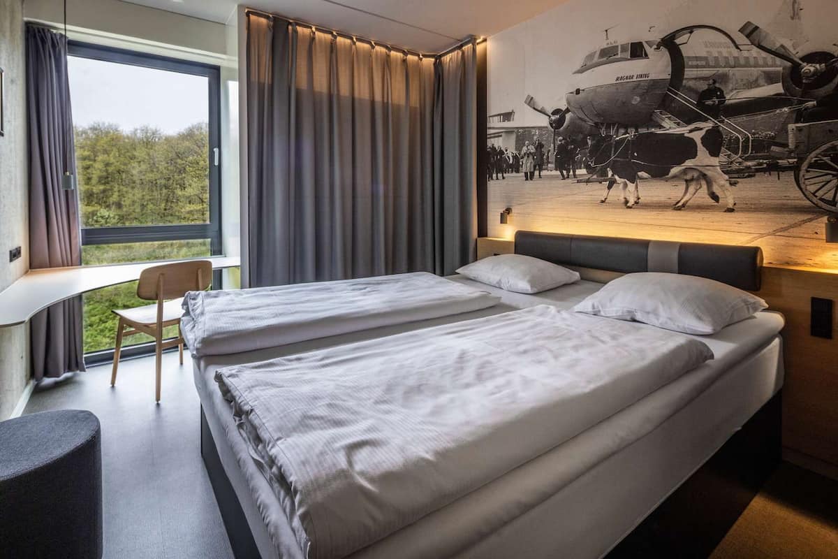 A modern hotel room with a large bed, a desk, and a window with curtains.