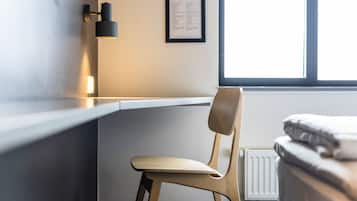 A modern room with a wooden chair, a white desk, and a bed with a white headboard.
