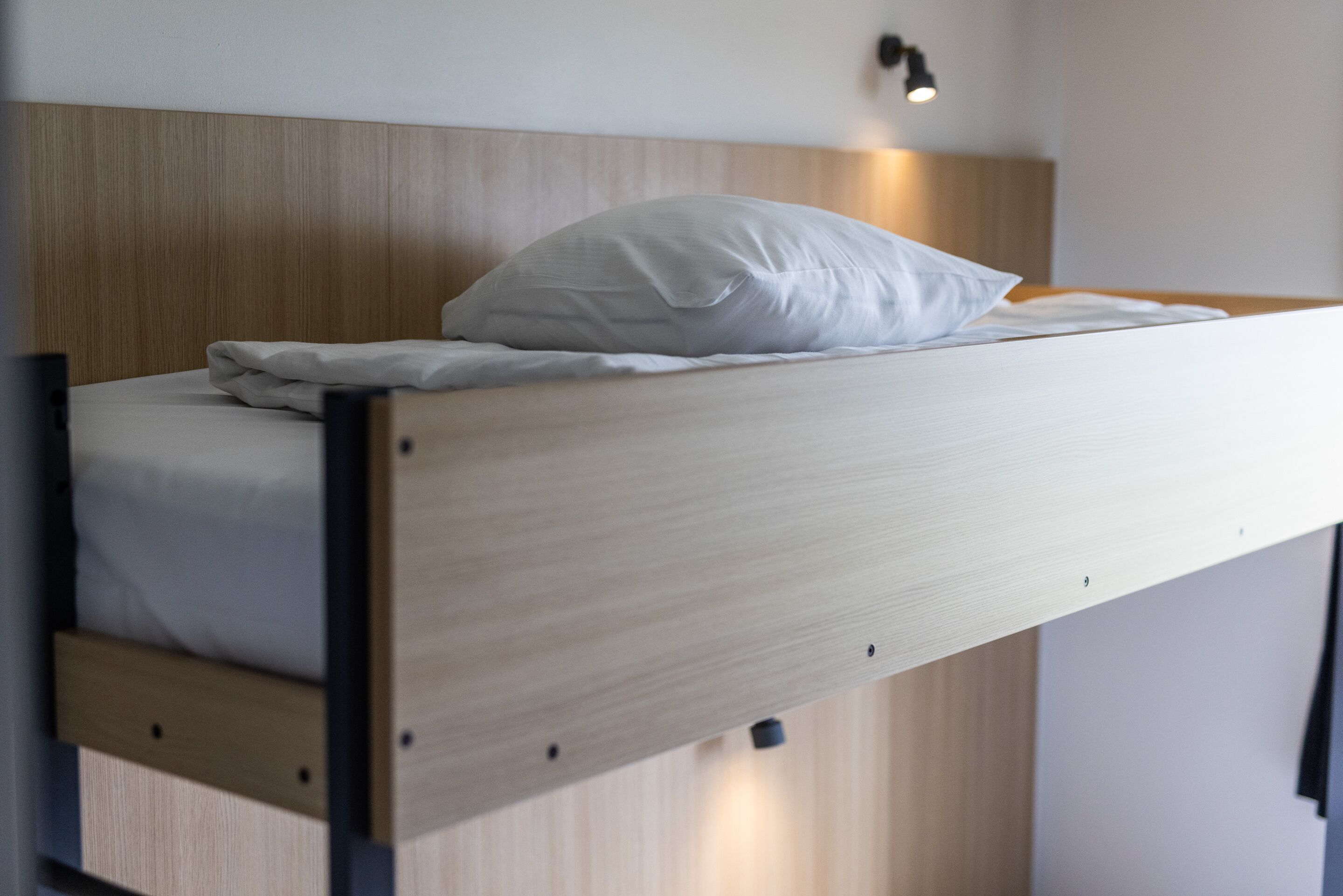 A bunk bed with a wooden headboard, a white pillow, and a bedside lamp.