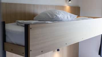 A bunk bed with a wooden headboard, a white pillow, and a bedside lamp.