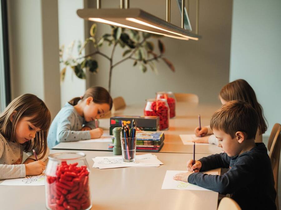 A dining table with children drawing, surrounded by books and jars of colored pencils.