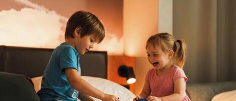 Two children playing with building blocks on a bed in a hotel room.