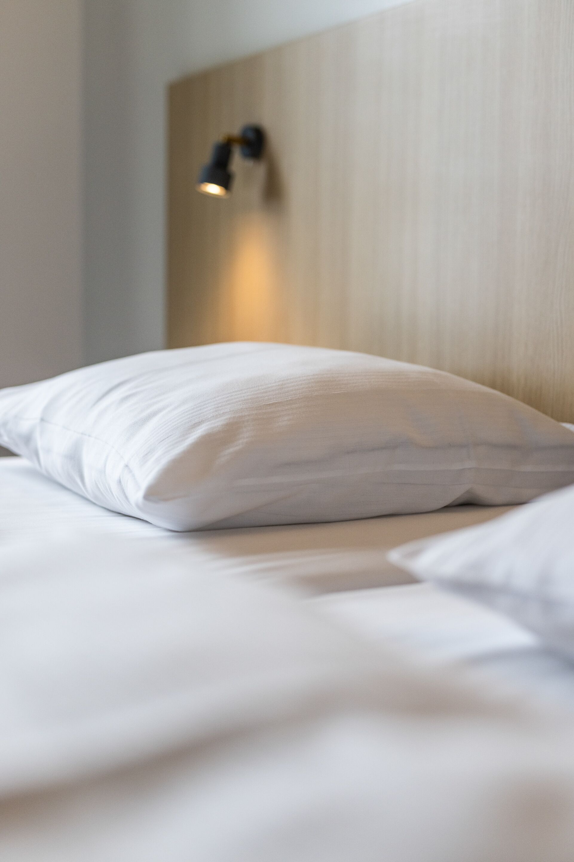 A neatly made bed with white bedding and a single white pillow.