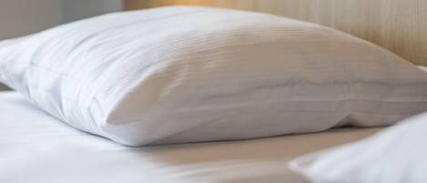 A neatly made bed with white bedding and a single white pillow.