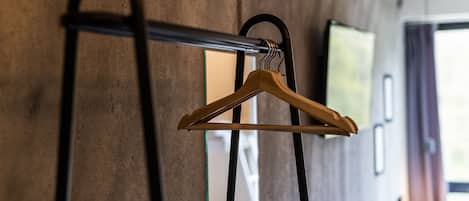 A wooden hanger on a metal rod against a textured wall, with a window and a framed picture in the background.
