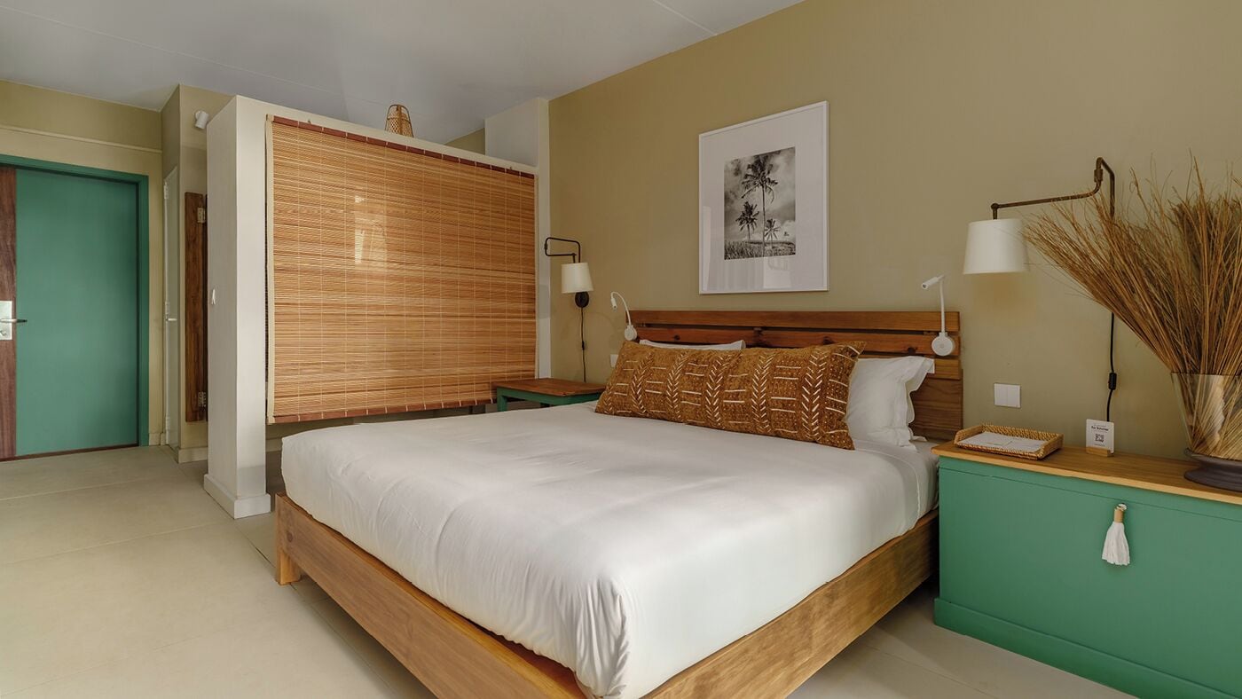 Une chambre à coucher avec un lit, des tables de chevet, une lampe fixée au mur, un tableau et une porte.