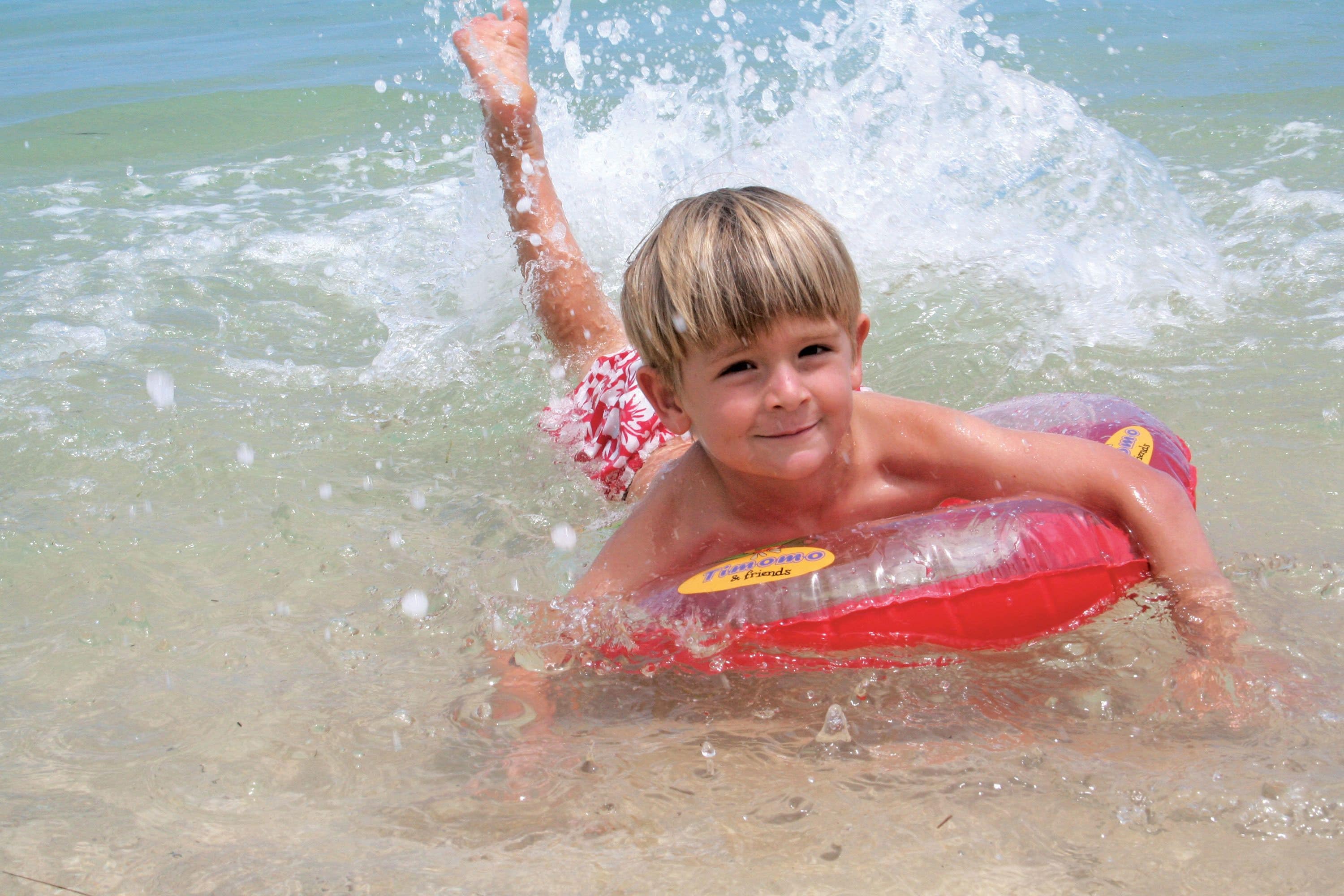 A child in a swimming pool using a red inflatable float with a yellow sticker.