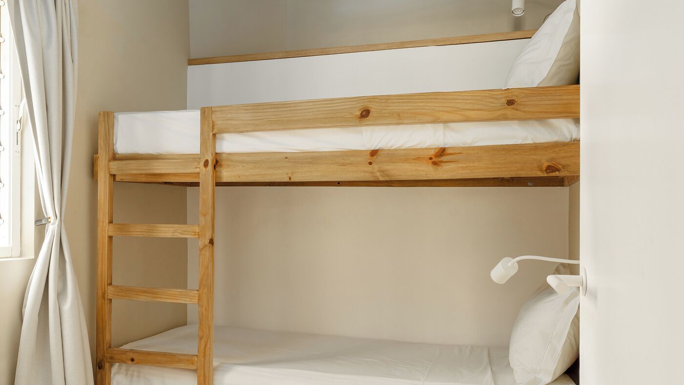 A bunk bed with a wooden ladder, white bedding, and a white wall.
