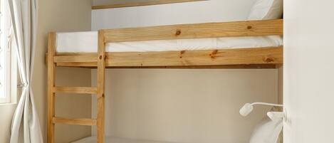 A bunk bed with a wooden ladder, white bedding, and a white wall.