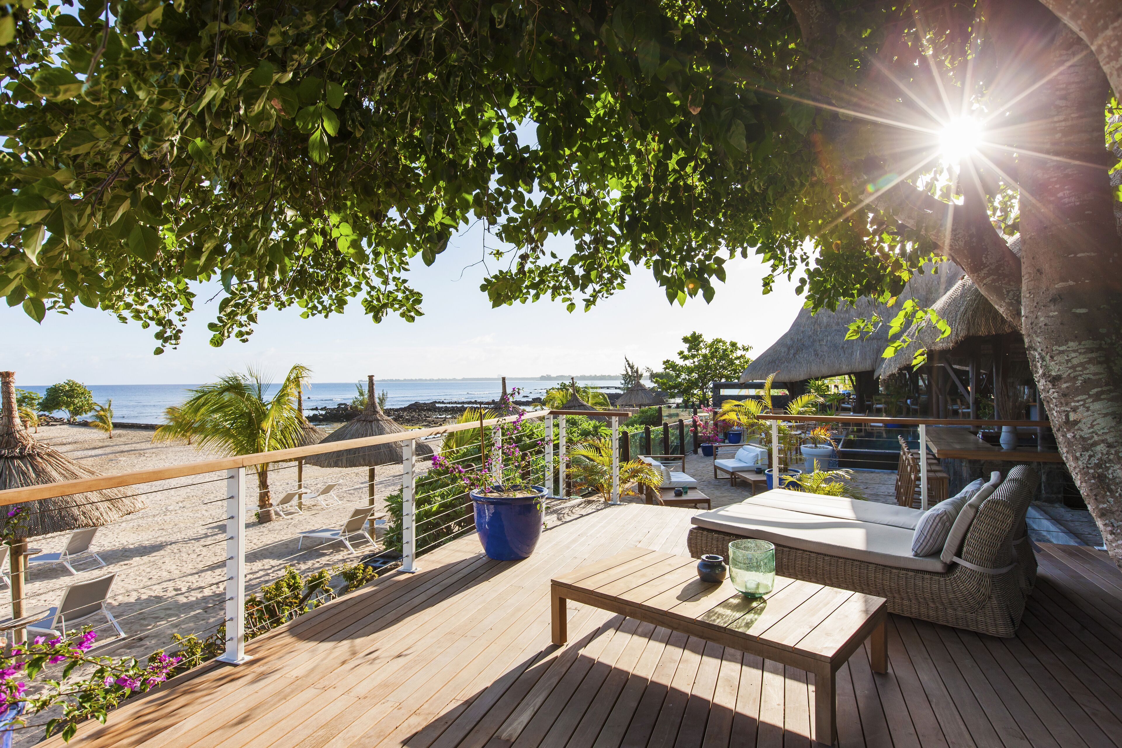 A wooden deck with lounge chairs and a table, overlooking a beach and ocean.