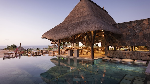 A poolside area with a thatched-roof structure, stone walls, and outdoor seating.