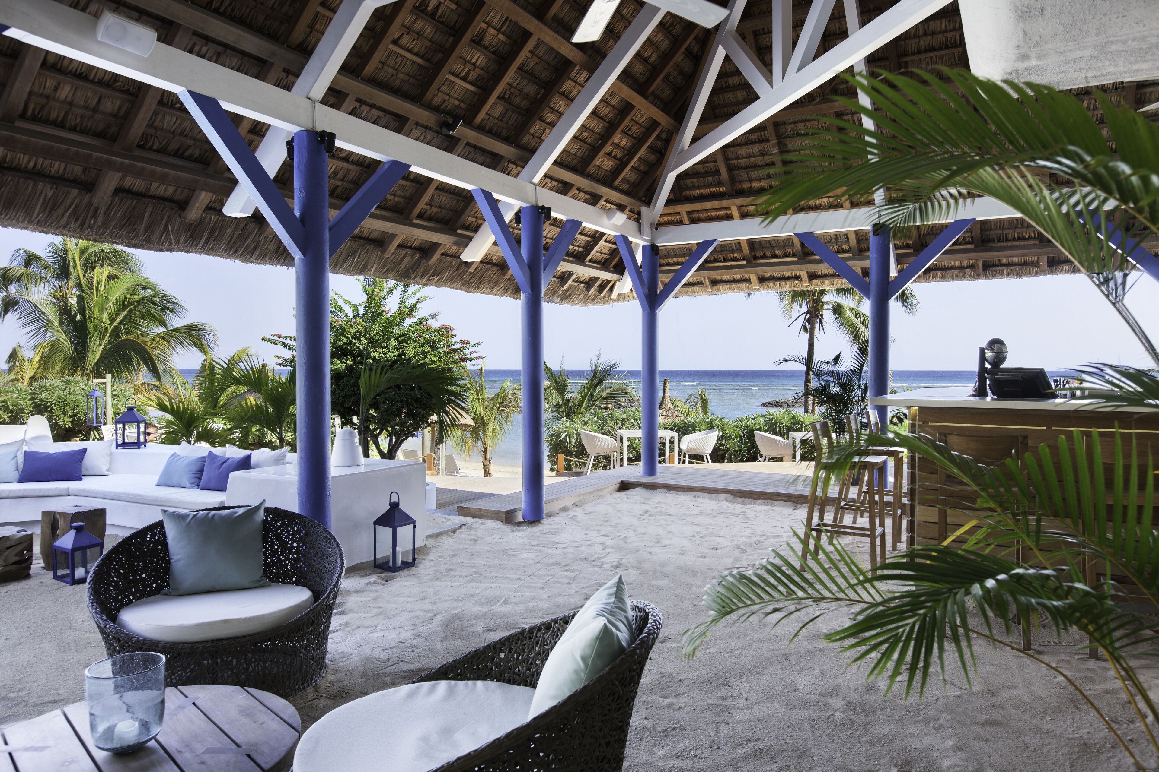 A beachside lounge with a thatched roof, white sofas, and blue accents.