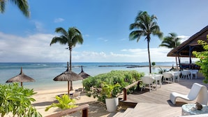 A wooden deck with white wicker furniture, palm trees, and a view of the ocean.