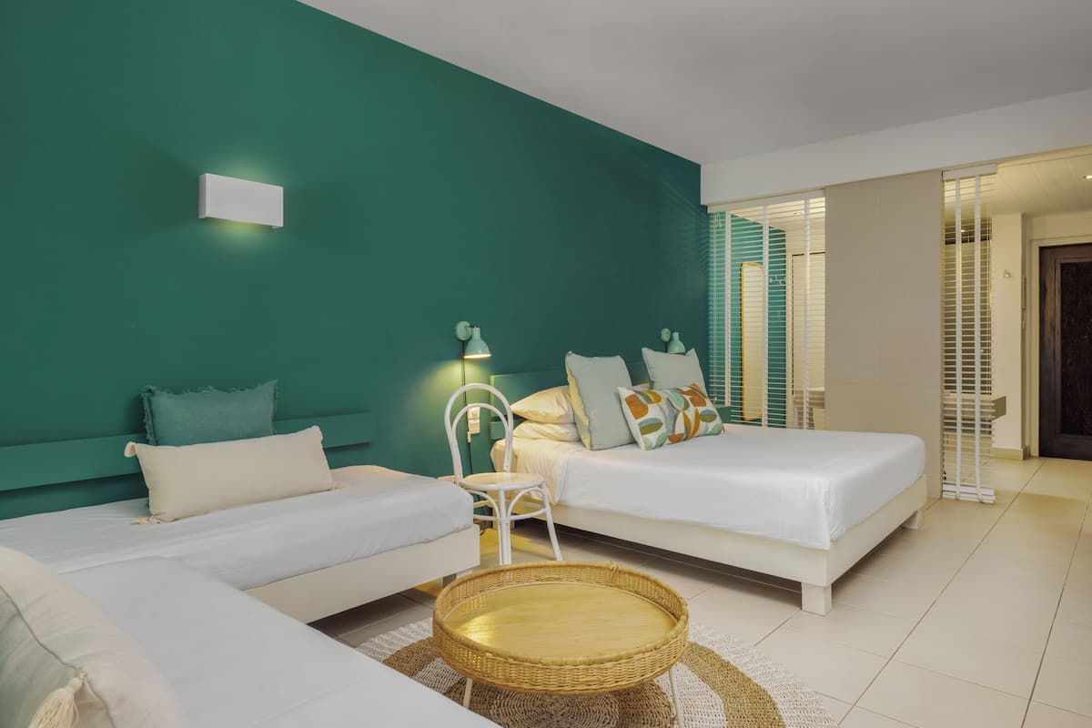 A modern hotel room with two beds, a wicker side table, and a teal accent wall.