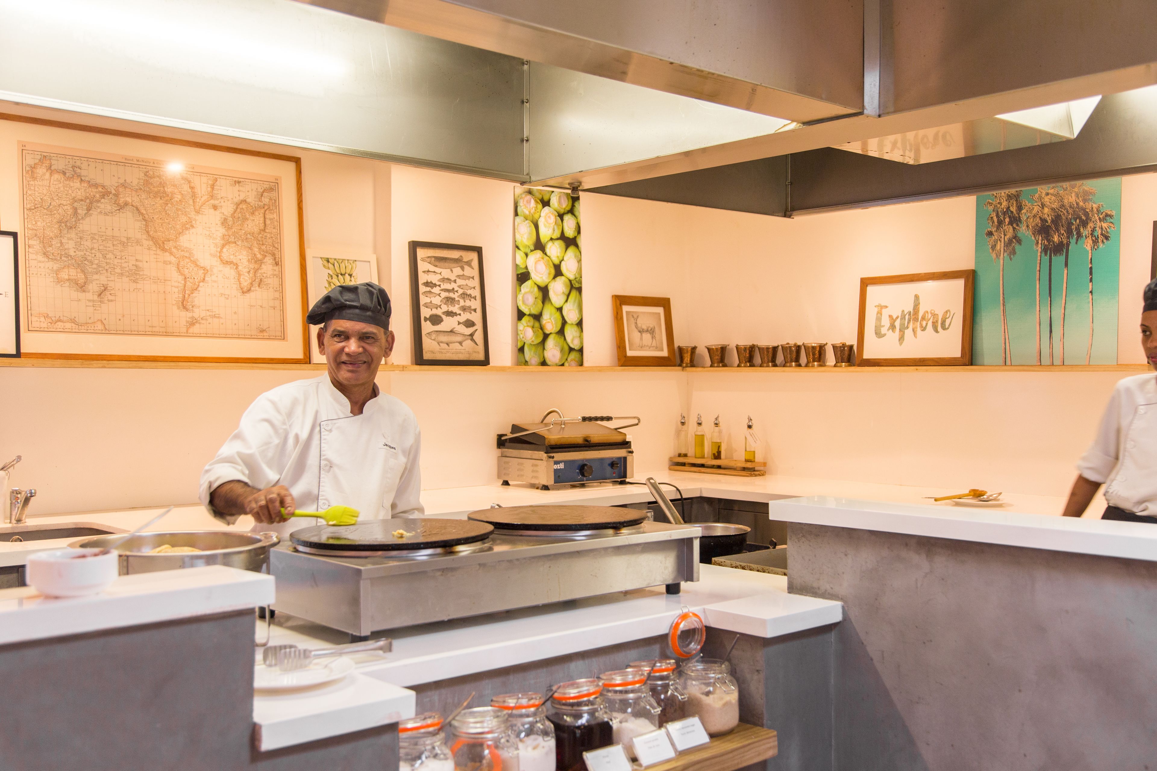 A kitchen with chefs preparing food, a world map, and a 'Explore' sign on the wall.