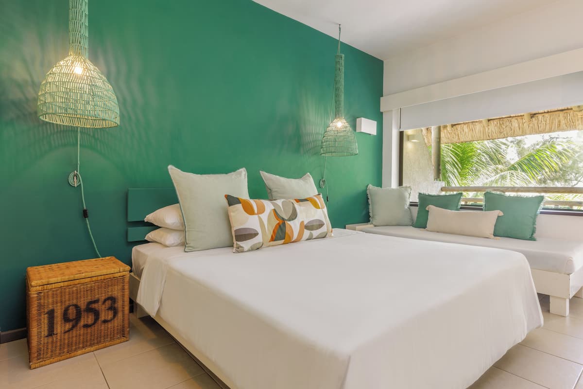 A hotel room with two beds, green walls, and a large window with a view of palm trees.