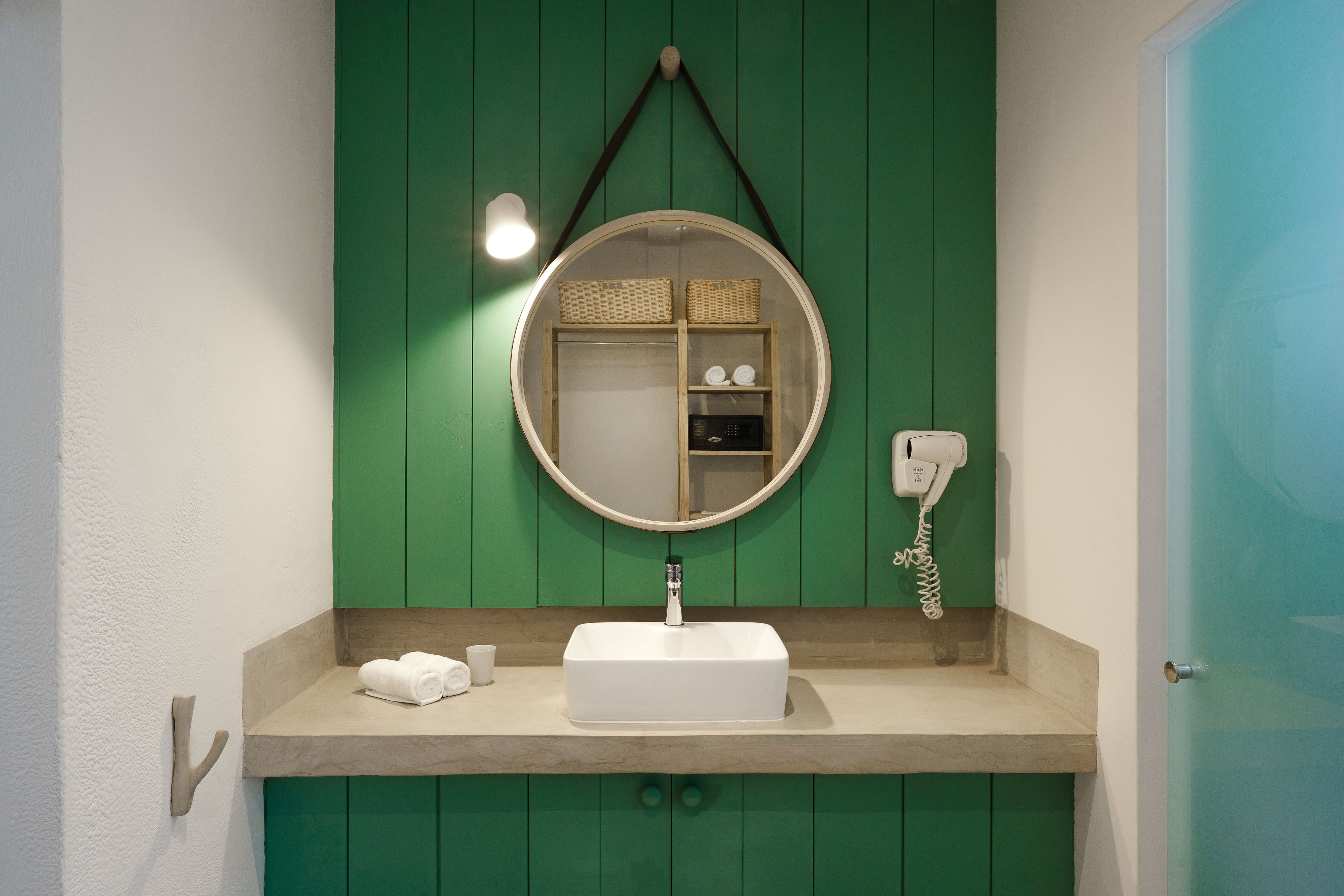 A bathroom with a green wall, a round mirror, a white sink, and a towel rack.