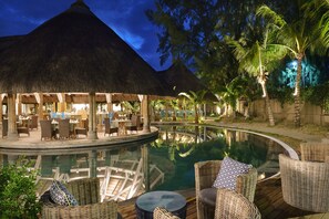A poolside area with thatched-roof structures, wicker furniture, and a clear pool reflecting the surroundings. - Coin de Mire Attitude (Cap Malheureux)