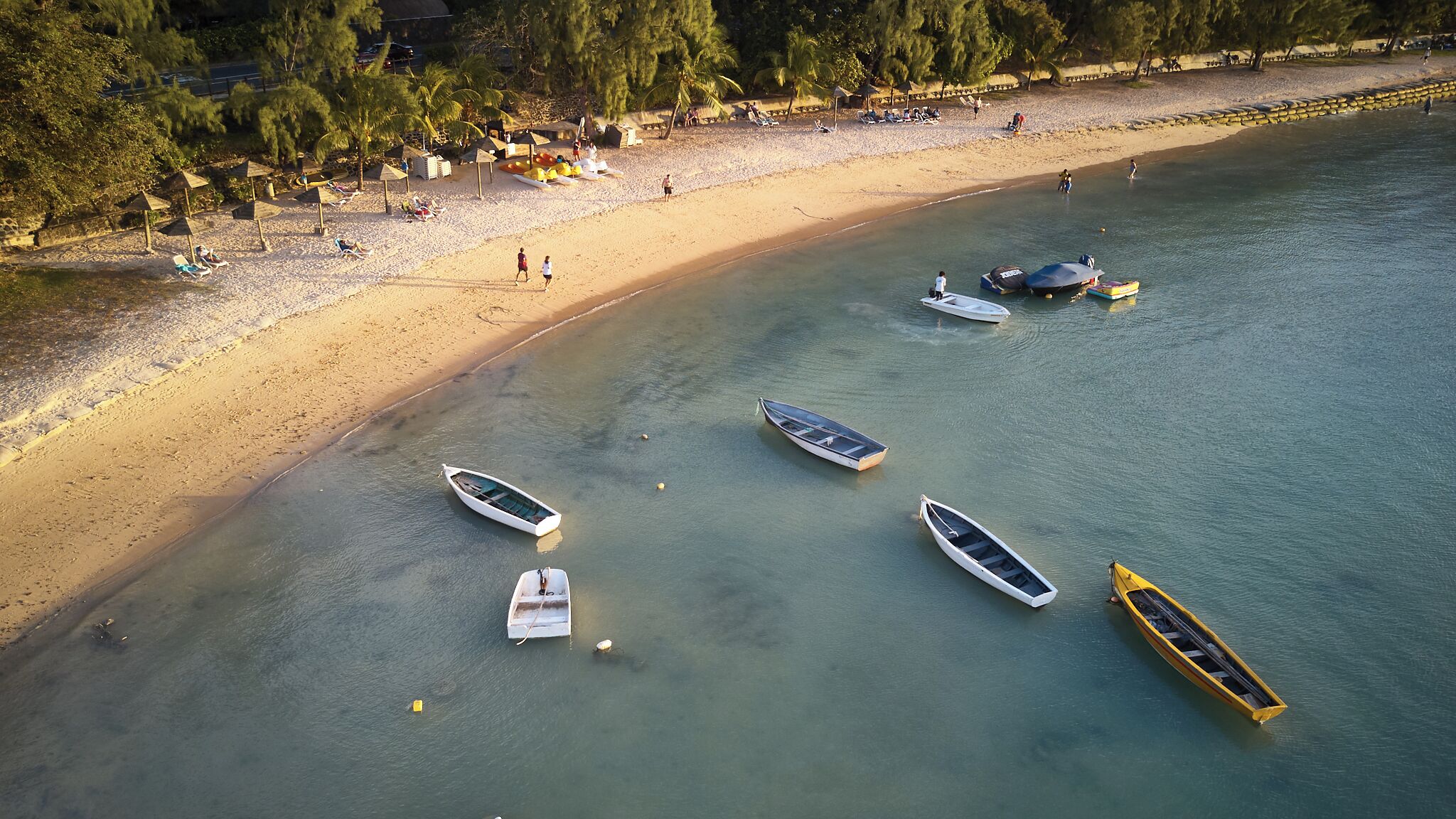 Eine Luftaufnahme eines Strandes mit mehreren Booten, die in der Nähe des Ufers vor Anker liegen, einem Sandstrand und einigen Spaziergängern.
