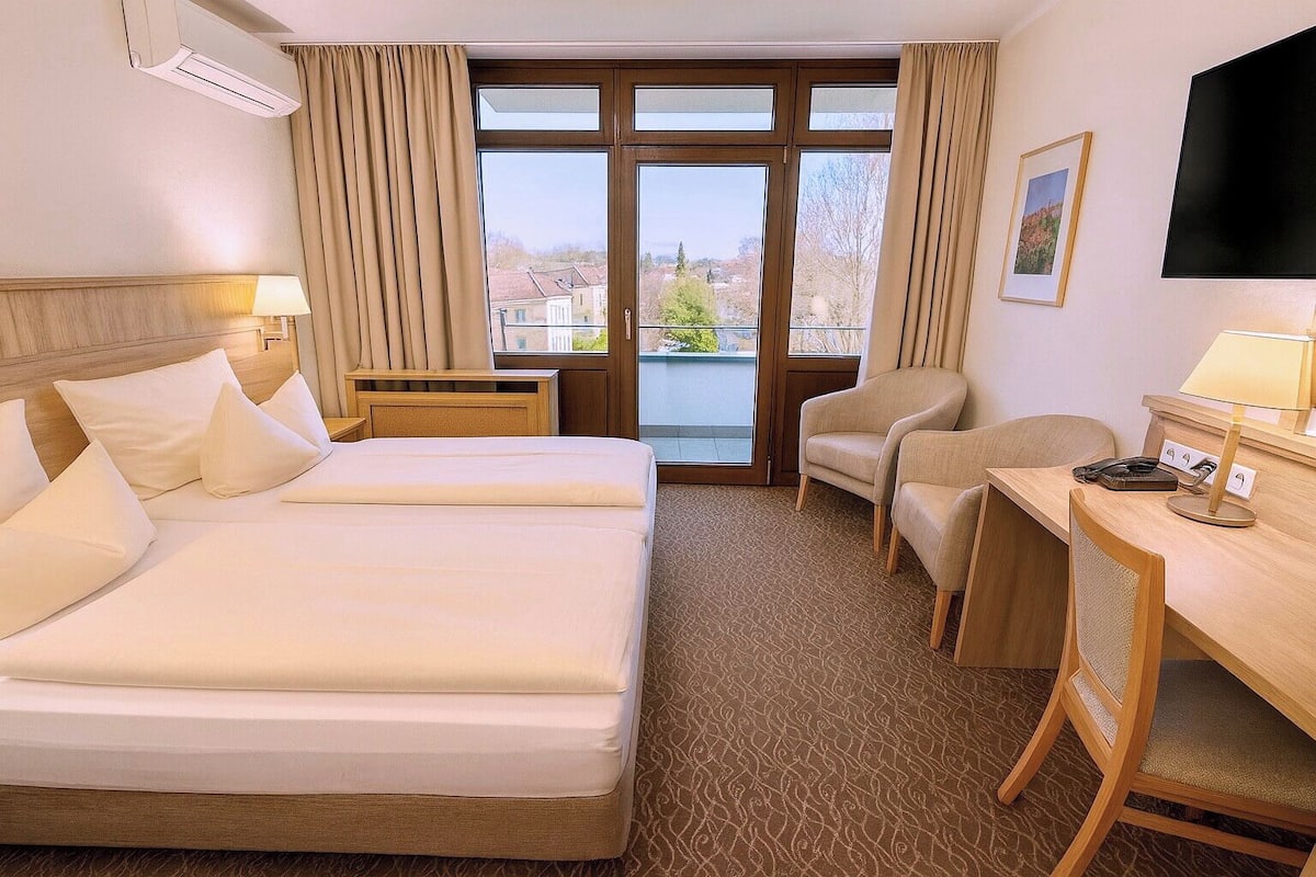 A hotel room with two beds, a desk, a chair, a TV, and a window with curtains.