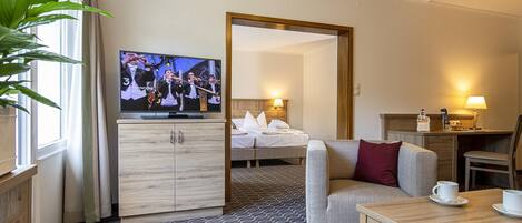 Habitación de hotel con cama, televisión, sofá, mesa con tazas y una planta.