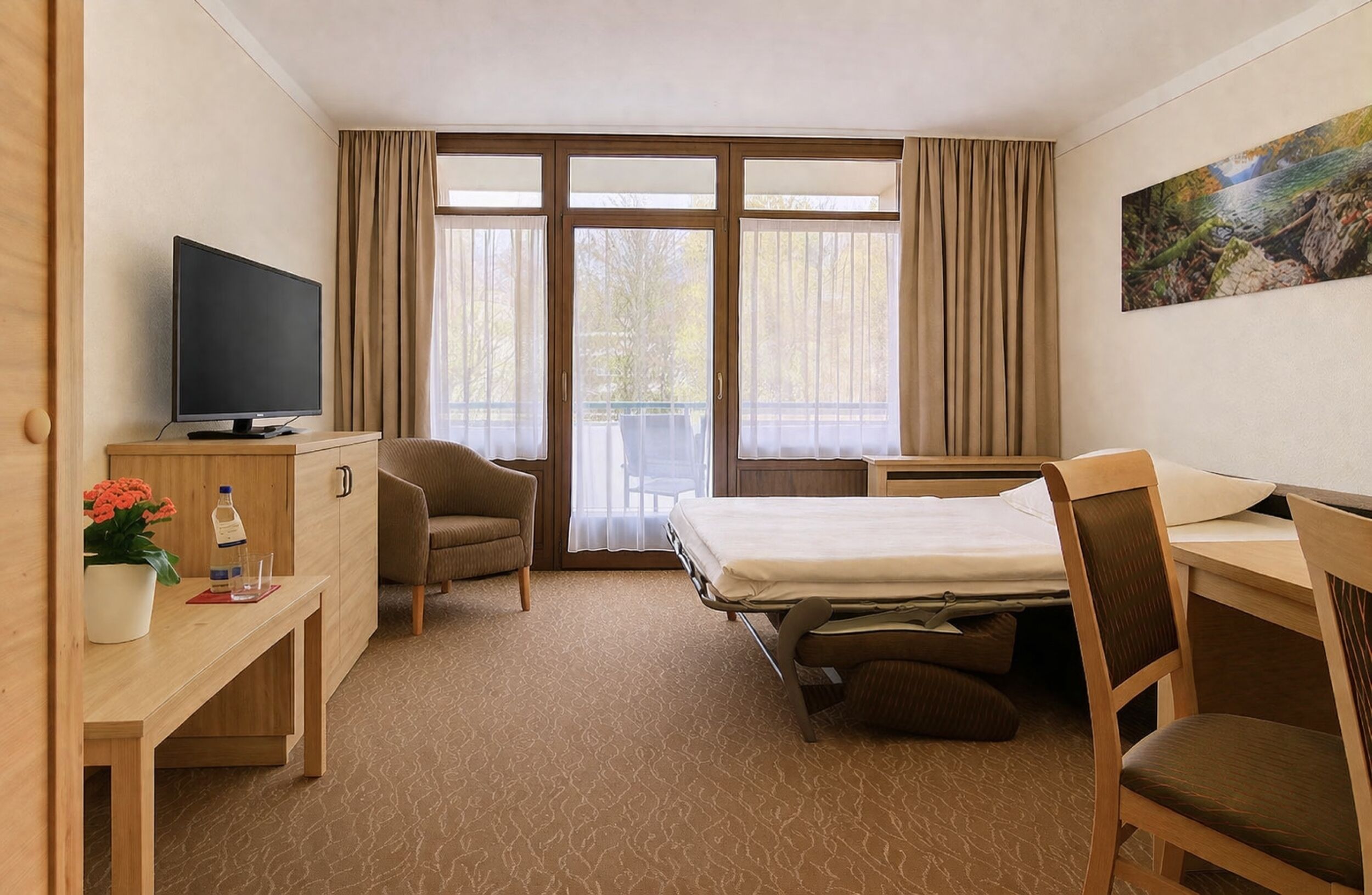 A hotel room with a bed, desk, chair, television, and a window with curtains.