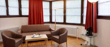 A room with a brown sofa, two armchairs, a small table with a tray, a floor lamp, and a coffee cart.