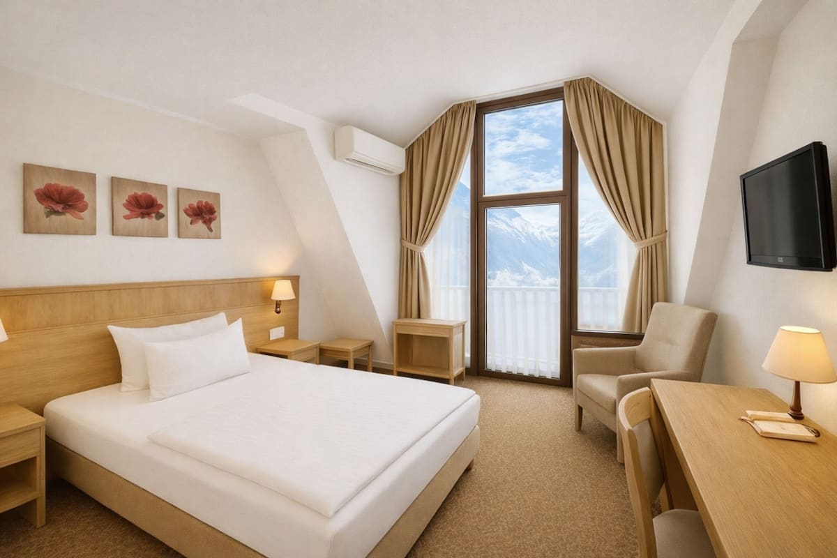 A hotel room with a large bed, a desk, a chair, a TV, and a balcony with curtains.