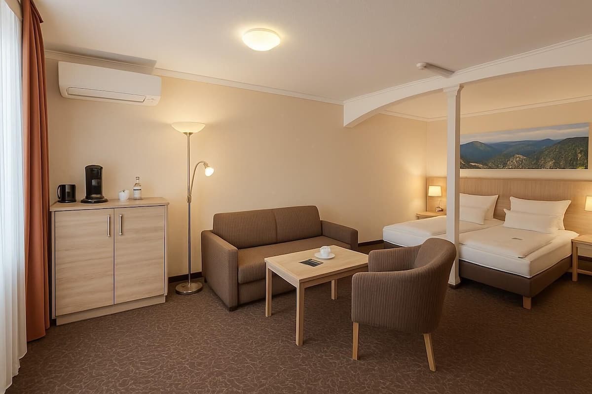 A hotel room with a bed, a sofa, a small table, a desk, a lamp, a cabinet, and a painting on the wall.