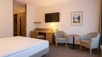 A hotel room with a bed, a desk with a chair, a small table with a chair, a TV, and a framed picture on the wall.