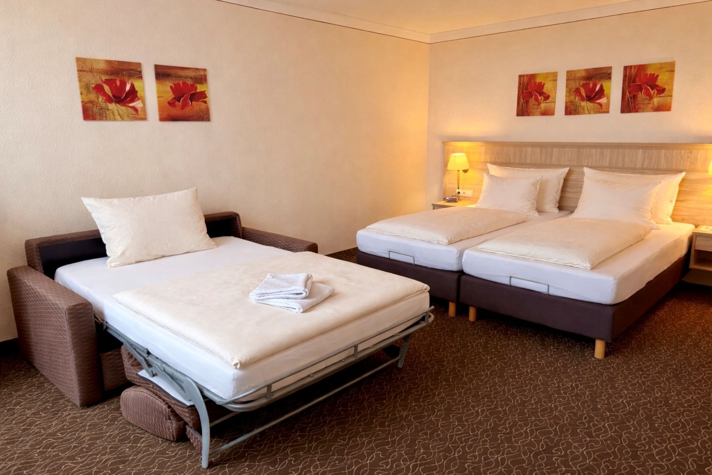 Habitación de hotel con una cama individual, un sofá, dos mesitas de noche y tres lámparas fijadas a la pared.