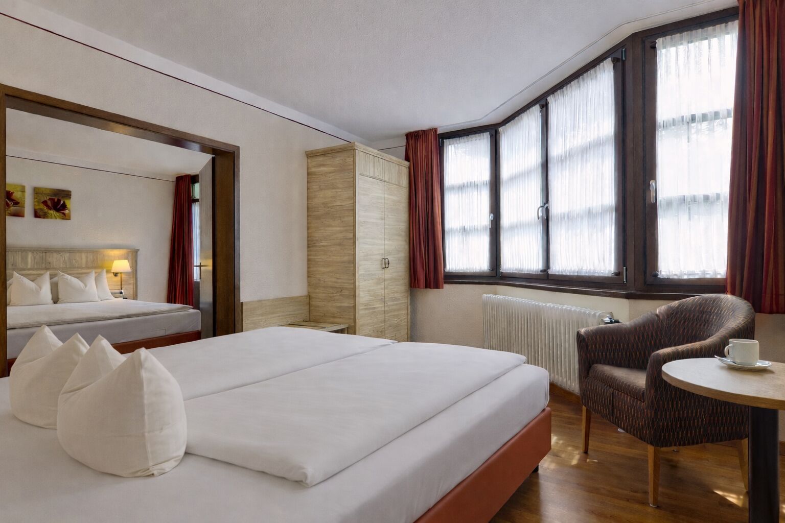 Une chambre d’hôtel avec un grand lit, une chaise, une petite table et une fenêtre avec des rideaux.