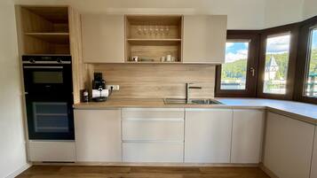 Eine moderne Küche mit integrierten Geräten, einer Kaffeemaschine und Blick auf eine grüne Landschaft durch ein Fenster.