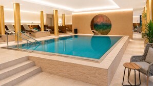 Una piscina con gradini, sedie a sdraio e un muro decorato con un'opera d'arte circolare.