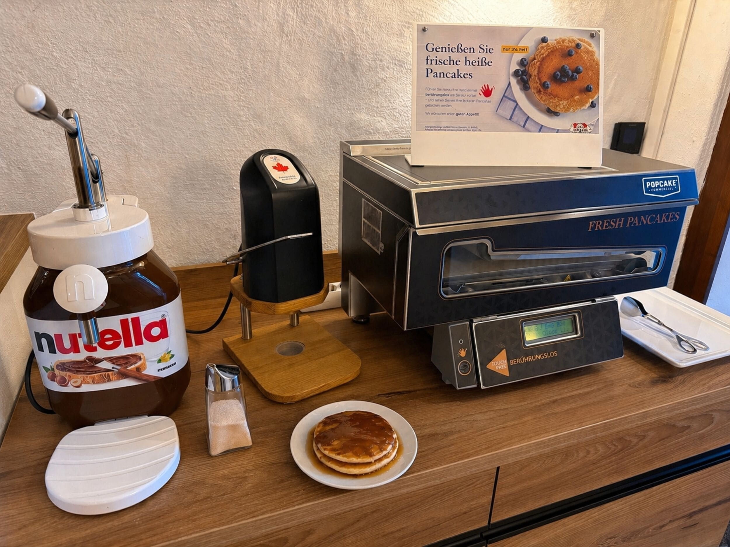 Un plan de travail de cuisine avec un distributeur de Nutella, un four professionnel pour faire des « popcakes » et une boîte de crêpes fraîches.
