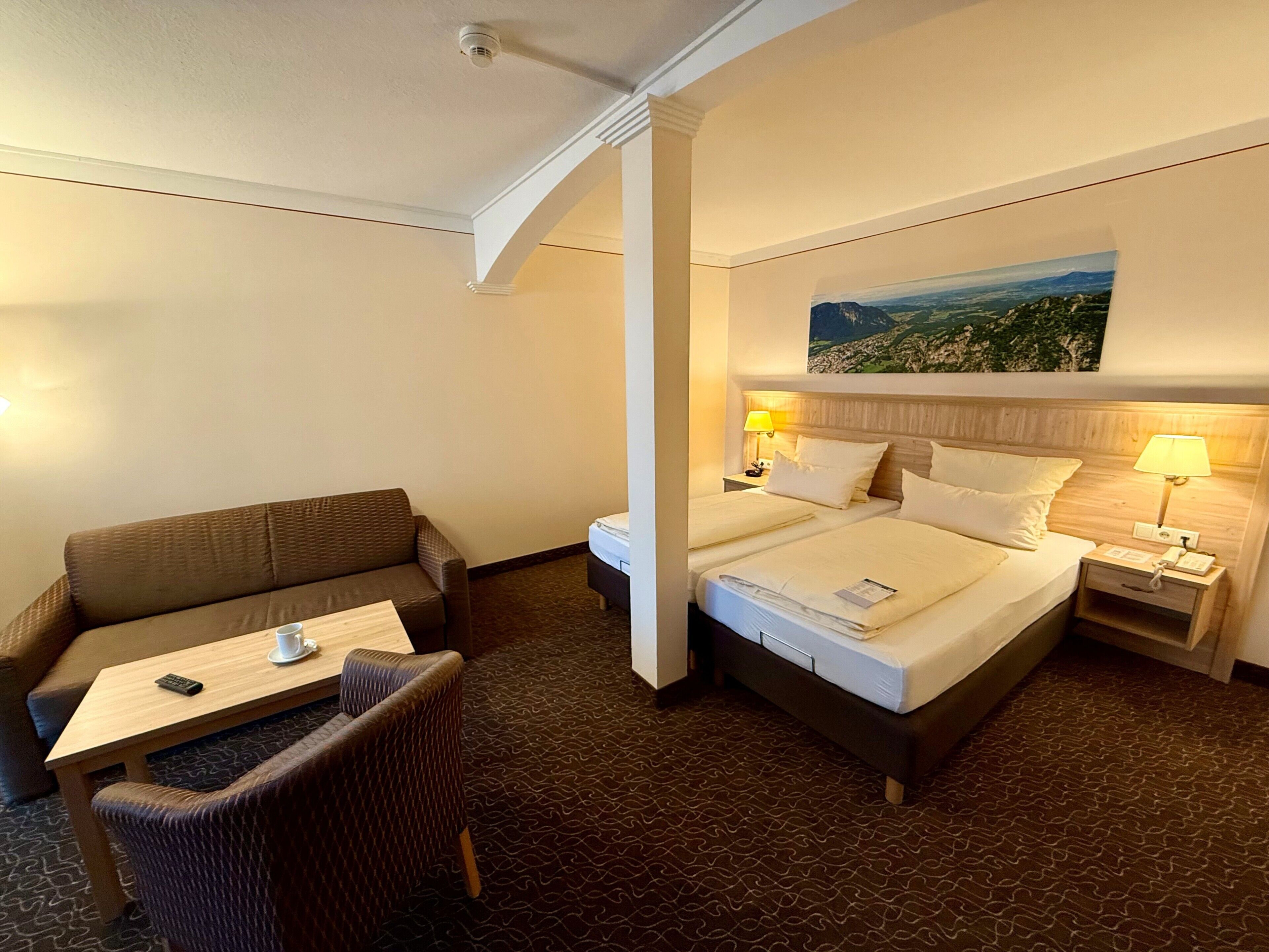 Una camera d'albergo con un letto, due comodini, un divano e un piccolo tavolino con un telecomando.