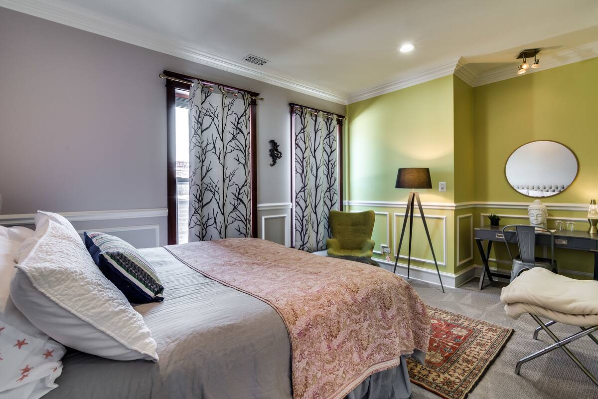 A bedroom with a bed, a desk, a chair, a lamp, and a mirror.