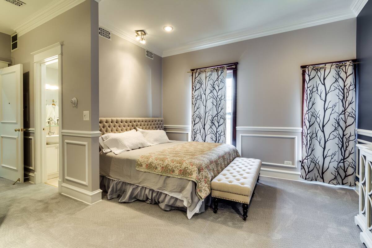 A bedroom with a large bed, a bench, and a walk-in closet.