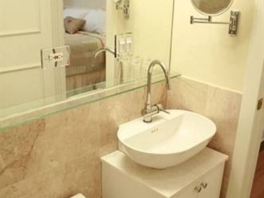 Un bagno con un lavandino bianco, cabina doccia in vetro, un water e uno specchio.