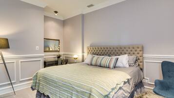 A bedroom with a tufted headboard, a bed with striped bedding, a blue armchair, and a small side table with a lamp.