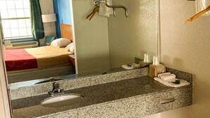 A hotel room with a bed, a bathroom with a sink, a mirror, and toiletries. - Luxury Inn & Suites Forrest City (Forrest City)