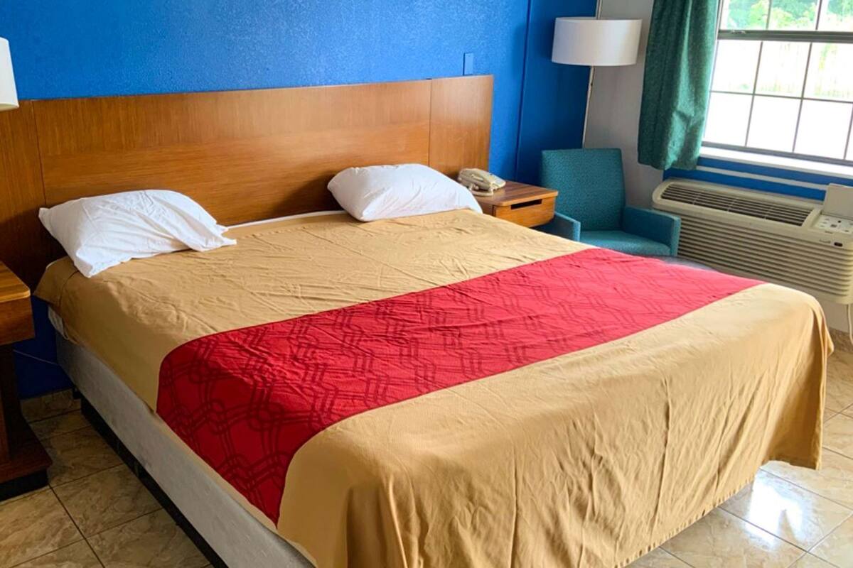 A hotel room with a bed, two bedside tables, a lamp, a chair, and a window with curtains.