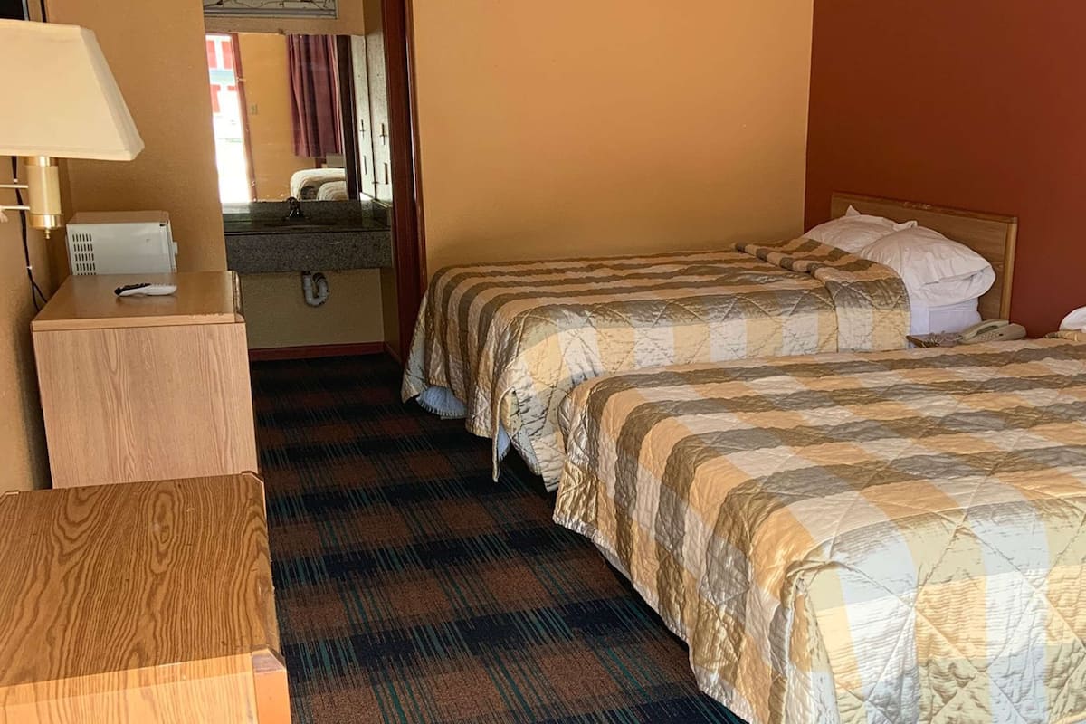 A hotel room with two beds, a wooden desk, a mirror, and a bathroom with a sink and towel rack.