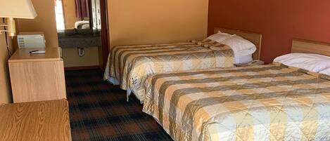 A hotel room with two beds, a wooden desk, a mirror, and a bathroom with a sink and towel rack.