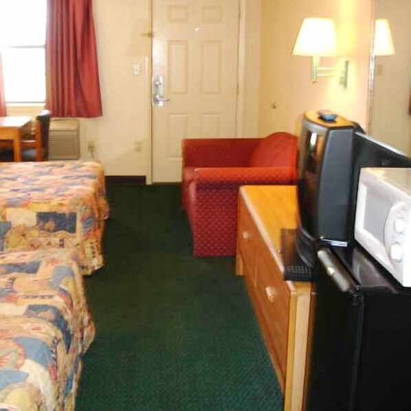 A hotel room with two beds, a television, a microwave, and a red chair.