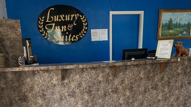 A reception desk with a sign reading "Luxury Inn & Suites," a framed painting, and a dog statue. - Luxury Inn & Suites Forrest City (Forrest City)