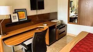 A hotel room with a wooden desk, a chair, a television, a small refrigerator, and a bed with a red blanket. - Luxury Inn & Suites Forrest City (Forrest City)