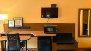 A compact hotel room with a wooden desk, a microwave, a small refrigerator, a television mounted on the wall, and a framed picture on the desk. - Luxury Inn & Suites Forrest City (Forrest City)
